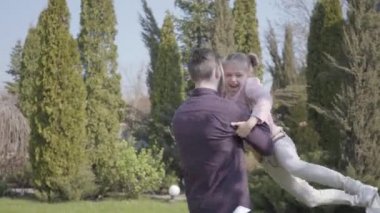 Neşeli genç baba kollarında dönüyor tatlı tatlı kızı ve güneşli bahar gününde eğleniyorlar.