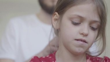 Portre genç sakallı baba küçük kızının saçlarını tararken çocuk aynanın önünde kabarık halıda yerde oturan oyuncaklarını tarıyor. Aile eğlencesi. Babalık, sevecenlik