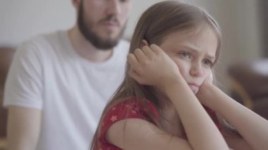 Ön planda oturan büyük güzel gözleri olan üzgün küçük kız başını yakın destekledi. Arka plandaki sakallı baba. Çocuk babasından rahatsız oldu. Çocuk yetiştirmede zorluklar