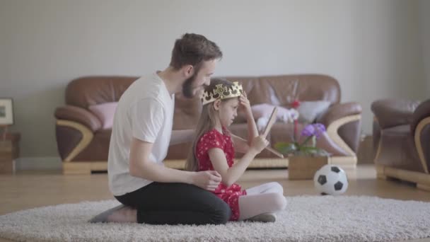 Portrait young handsome father dressed his cute little long-haired daughters head with crown and she is happy — Stock Video