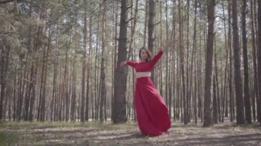 Ormanda dans eden kırmızı elbiseli genç bir kadın. Güzel dansçı çam arasında çağdaş dans. Kadın hassasiyeti ve uyum yaşam kavramı.