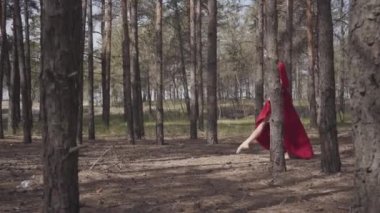 Orman manzarasında dans eden kırmızı elbiseli zarif kadın. Güzel çağdaş dansçı. Zarif kız koşar ve atlar. Kamera kızla paralel hareket ediyor. Yandan çekim.