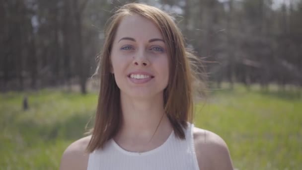 Retrato de una linda y graciosa chica sonriente con el pelo soplando en el viento. Hermosa tierna morena deportes al aire libre . — Vídeo de stock