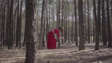 Ormanda dans eden kırmızı elbiseli profesyonel genç kadın. Ağaca dokunan güzel bir kadın. Kadın hassasiyeti ve uyum yaşam kavramı. Muhteşem etkileyici bir manzara. Yavaş çekim
