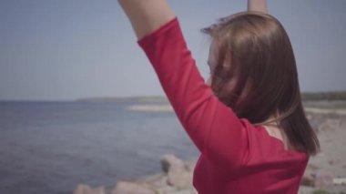Kırmızı uzun elbise dans yakın portre sevimli graseful kadın mavi deniz suyu ve şaşırtıcı gökyüzü muhteşem görünümü ne yakın büyük taş üzerinde el kaldırır. Çağdaş dansçı açık havada. Yavaş çekim.