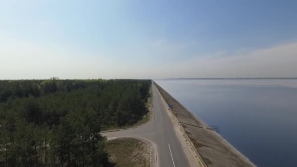 Vista superior do dron da incrível floresta verde à esquerda, lago azul à direita e longa estrada reta no meio. Natureza espetacular . — Vídeo de Stock