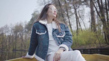 Güneş gözlüğü ve bir göl veya nehir üzerinde bir tekne üzerinde yüzen bir kot ceket görkemli bir genç kadının portresi. Güzel esmer aktif bir gün kapalı rahatlatıcı ya da doğanın tadını çıkararak seyahat.