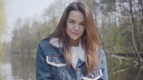 Portret van mooie jonge lachende vrouw die in de camera kijkt. Mooi landschap, rivier op achtergrond — Stockvideo