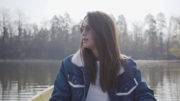 Portret mooie glamour vrouw in witte broek, jeans jasje en zonnebril peddels op de gele boot op de rivier, rond te kijken. Meisje leren roeien. Verbinding met de natuur. Actieve levensstijl — Stockvideo