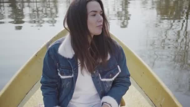 Portret uroczej młodej kobiety ubrana w dżinsową marynarkę pływającą na łodzi na jeziorze lub rzece. Piękna Brunetka aktywnie relaksująca się na dzień lub podróżując ciesząc się naturą. — Wideo stockowe