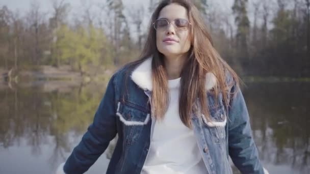 Porträt einer jungen Glamour-Brünette mit modischer Brille und Jeansjacke, die in die Kamera blickt. schöne Landschaft im Hintergrund — Stockvideo