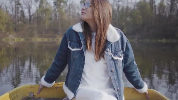 Portrait pretty young woman in fashionable glasses and jeans jacket looking in the camera. Beautiful landscape on background — Stock Video
