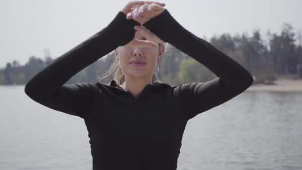 Portrétní okouzlující, štíhlá žena, která dělá sportovní cvičení, stojí na břehu řeky. Krásná krajina na pozadí. Volný čas venku, aktivní životní styl, cvičení. — Stock video