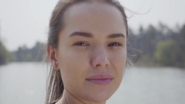 Feche o retrato de uma jovem mulher sorridente bonita com rabo de cavalo olhando para a câmera. Bela paisagem, rio no fundo — Vídeo de Stock