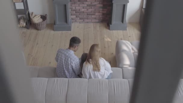 Beautiful young international family at home, african american man, caucasian woman and small girl sitting on the sofa in large living room. Top view, shooting from above. — Stockvideo