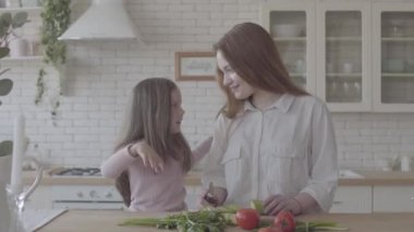 Portre güzel genç anne ve büyük mutfakta onun sevimli küçük kızı, kadın yemek ve küçük kız onu öpmek