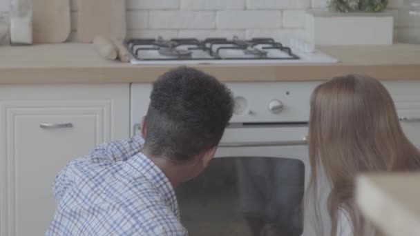 Schienale di donna con lunghi capelli biondi e giovane uomo seduto sul pavimento e guardando il forno . — Video Stock