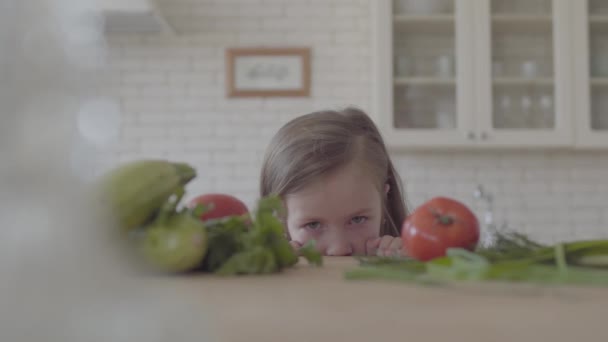 Świeże cukinia warzywna, pomidory i zielenina układania na stole. Cute Little Girl patrzy z tabeli, ukrywając patrząc w aparacie. Zdrowy styl życia — Wideo stockowe