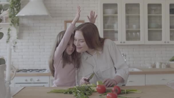 Портрет очаровательный молодой матери и ее милая маленькая дочь на большой кухне, женщина приготовления пищи и маленькая девочка поцеловать ее — стоковое видео