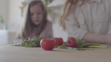 Masada sebze, domates, soğan ve yeşillik kapatın. Arka planda kadın ve küçük bir kız silueti. Aile ilişkileri.