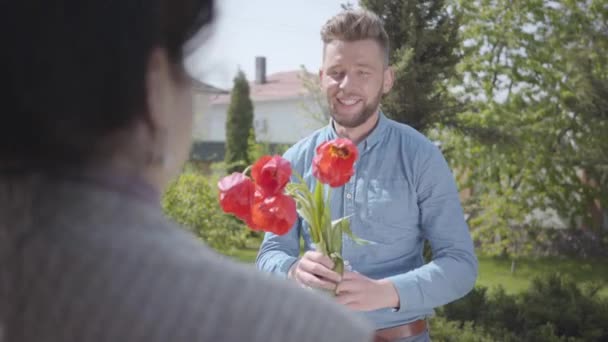 Pohledný vnuk navštívil svou babičku a přinesl jí kytici tulipány. Vousatý muž objal svou babičku. Lidé se usmívají. Žena, která někoho pozvala. Rodinný vztah, narozeniny — Stock video
