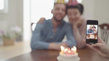 Kadın el yetişkin torunu ile sarılma mutlu gülümseyen olgun kadın cep telefonu bir fotoğraf yapma, doğum günü kapakları hem de. Pasta insanların önünde masada. Büyükannenin doğum günü