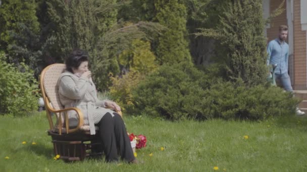 Volwassen kleinzoon een bezoek aan zijn grootmoeder, het brengen van haar boeket van tulpen. De bebaarde man die het huis binnenkomt en zijn oma knuffelen. Mensen glimlachen. Familie relatie — Stockvideo