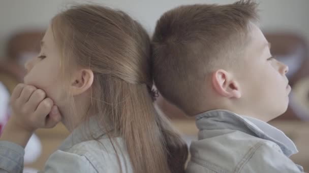 Close up ritratto gemello ragazzo e ragazza si siedono sul pavimento del soggiorno schiena a schiena arrabbiata tra loro. Una relazione tra fratello e sorella. Il concetto di amore familiare per bambini . — Video Stock