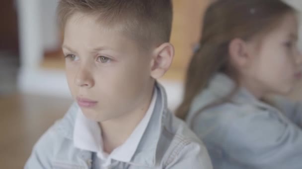 Küçük erkek ve kız kardeş ikizler rahatsız ve hoş olmayan yüzleri ile birbirlerine sırtlarını kızgın oturup — Stok video