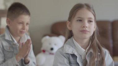 Portre sevimli ikiz kardeşi yaramaz çocuk onun sevimli kız kardeşinin saçlarını çekerek ve rahat oturma odasında gülümseyerek oynarken