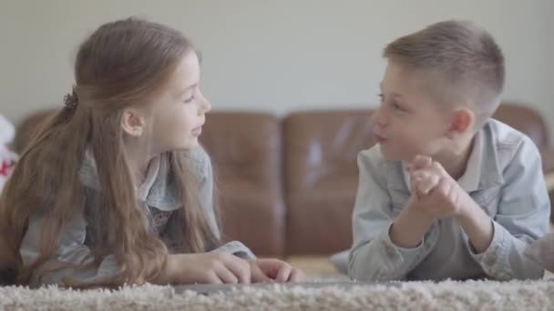 Söta små tvillingar pojke och flicka ligger på mattan och talar om något roligt att spela, skratta och leende — Stockvideo