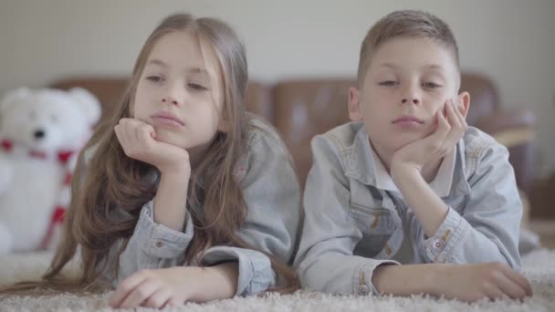 Portret tweeling liggend op het tapijt en vervelen en vervolgens op hetzelfde moment kijken naar elkaar. — Stockvideo