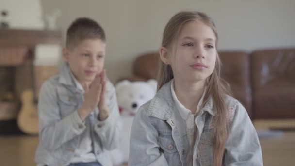 Portrét rozkošného dvojníka, nemravného chlapce, který si vytahuje vlasy své roztomilé sestry a usmívá se v útulném obývacím pokoji — Stock video