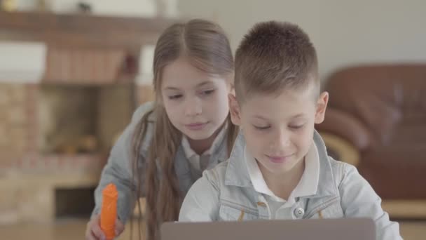 Portre sevimli küçük çocuk dizüstü bilgisayar ve küçük kız oturup, onun ikiz kardeşi evde sabun kabarcıkları darbe — Stok video