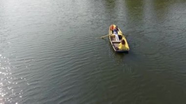 İki genç güzel kız güzel yansıtıcı göl veya nehir ortasında küçük tekne tekne vardır. Bir kadın kürek çekiyor. Aktif yaşam tarzı. Drone çekim, üstten görünüm, havadan çekim