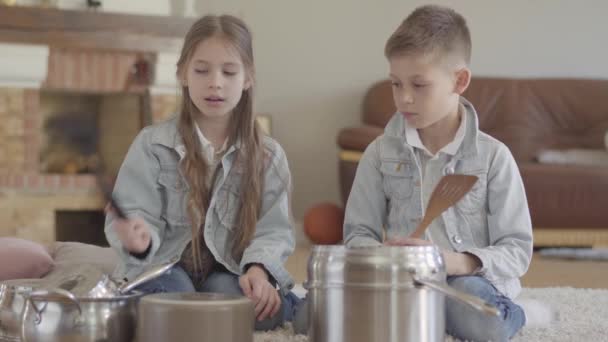 Portre sevimli sevimli erkek ve kız kardeşi ikiz büyük kaşık ve eğlenmek gülmek ile tencere ve yemekleri yenerek müzisyenler oynuyor — Stok video