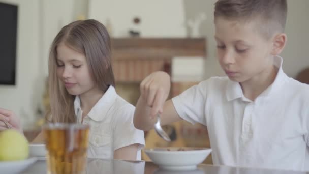 学校の前に欲望なしで朝食のためにおいしいお粥やコーンフレークを食べない兄弟姉妹の双子の肖像画 — ストック動画