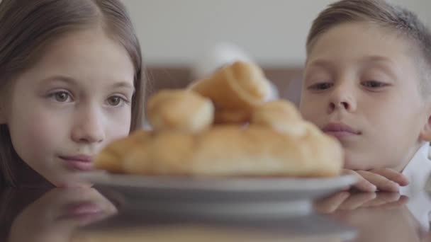 Nahaufnahme Porträt zweier entzückender Zwillinge, Bruder und Schwester, die mit Croissants ins Flugzeug schauen und sich vor Hunger die Lippen lecken — Stockvideo