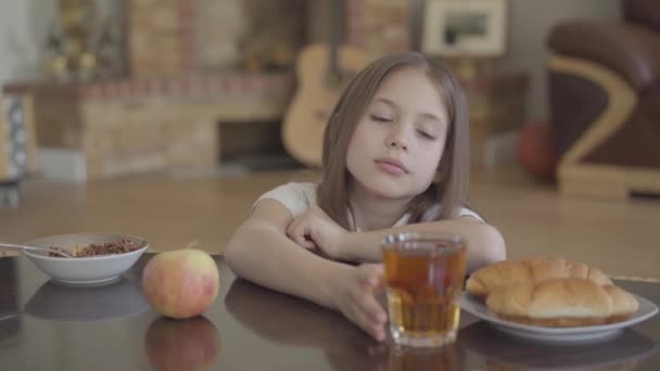 En la madrugada antes de la escuela, una chica linda y cansada se queda dormida en el desayuno cerca de muesli, croissant y jugo — Vídeos de Stock