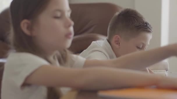 Крупним планом портрет сестри та її втомленого брата-близнюка, що проходить через блокноти з домашнім завданням, виснаженим після школи — стокове відео