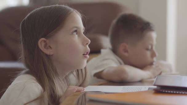 Närbild porträtt av tvillingsyster och hennes trötta bror tvilling blädderblock genom anteckningsböcker med läxor utmattad efter skolan — Stockvideo
