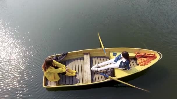 Due giovani belle ragazze sedute nella piccola barca nel bel mezzo di un bellissimo lago o fiume riflettente. Stile di vita attivo, connessione con la natura. Vista laterale — Video Stock