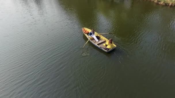 Twee jonge mooie meisjes varen in de kleine boot in het midden van een prachtig reflecterend meer of rivier. Een vrouw is peddelen. Actieve levensstijl. Drone schieten, bovenaanzicht, lucht schieten — Stockvideo