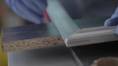 Mdf plakası üzerindeki çizgiyi işaretleyen eldivenli marangozun elleri kesilmelidir, sonra tahtayı alır. Yakından görüş. Çalışma süreci. El üretimi kavramı