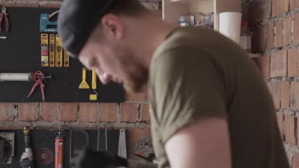 Perfil de cerca del electricista barbudo adulto que trabaja con detalles parados en la mesa en el garaje. Un hombre trabaja en un taller. El tablero con las herramientas colgando en la pared. Vista lateral — Vídeos de Stock