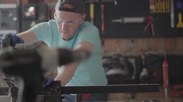 Portret vaardigheid man in bescherming glazen snijden van een houten bord met een kleine cirkelvormige zaag op de tafel in de workshop. Meubelfabriek. Concept van hand productie. Craftman werkt in een workshop. — Stockvideo