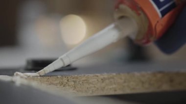 Tutkal tabancası siyah lamine partikül tahtasına yapıştırıcı koymuş. El imalatı. Craftman bir atölyede çalışıyor.