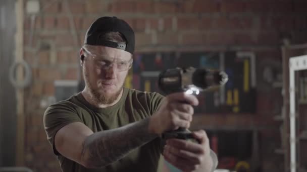 Bebaarde timmerman staande met speeder moersleutel schroevendraaier in de werkkamer en spelen met fasteting gereedschap zoals het is een pistool. Hand productie. Craftman werkt in een workshop. — Stockvideo