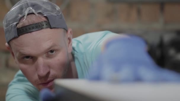 Retrato de cerca del hombre concentrado en la tapa, involucrado en su trabajo. El trabajador con guantes comprobando y midiendo su bricolaje. Profesión del carpintero. Concepto de fabricación manual. Trabajos de artesano — Vídeo de stock