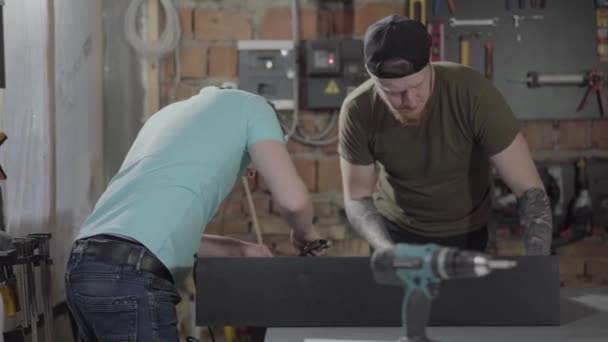 Dos tipos trabajando en un pequeño taller con herramientas. Dos carpinteros hacen piezas de madera con sus herramientas. Concepto de fabricación manual. Artesano trabaja en un taller . — Vídeos de Stock